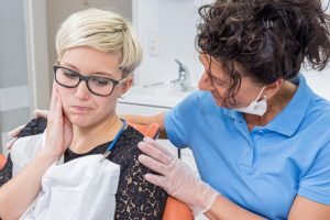 a woman holding her cheek in pain while a dentist comforts her