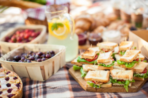 Close up of picnic blanket full of lemonade, fruit, sandwiches, etc.